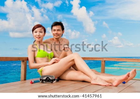 An attractive couple sitting on a wooden boat in the ocean