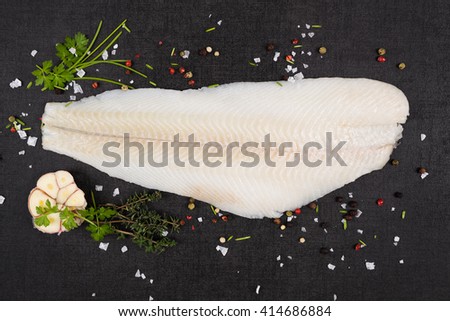 Fresh halibut fillet with fresh herbs and garlic on dark black stone background top view. Luxurious seafood eating background. 