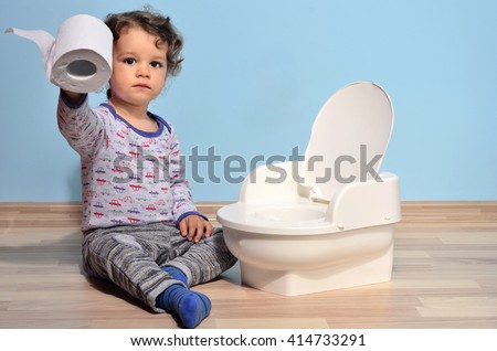 Cute kid potty training for pee and poo.Baby toddler sitting on the floor near a potty and playing with toilet paper Royalty-Free Stock Photo #414733291