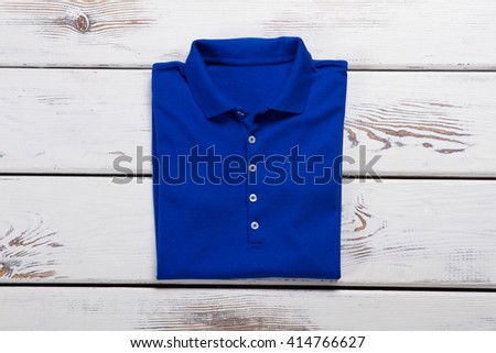 Blue folded polo t-shirt. Folded t-shirt on wooden background. Marketable condition of clothes. New high-quality garment.