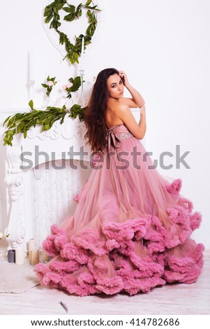 Fashion portrait of elegant woman with luxuriant hair. Brunette girl. Perfect makeup. A girl in a pink dress on a white background
