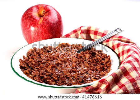 Chocolate cereals with milk in a deep soup plate, the checkered napkin and a red apple nearby lies. Recommendations for those who grows thin or the vegetarian.