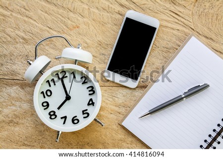 ball pen, smartphone, open notebook and alarm clock on wood table texture background top view