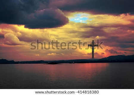 The Cross of Jesus Christ and beautiful dramatic clouds in the sunset with water reflection