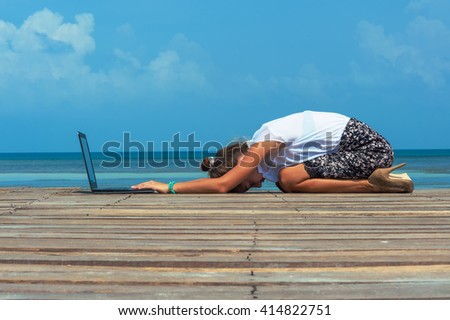 Woman in office suit doing yoga on the wooden floor with laptop. Young Lady has practice on the beach in front of sea view.