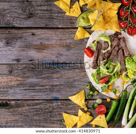 Food background with nachos chips and ingredients for making tortilla. Onion, tomatoes, chili peppers, beef, tortillas and corn with deeps over old wooden surface. Flat lay with copy space.