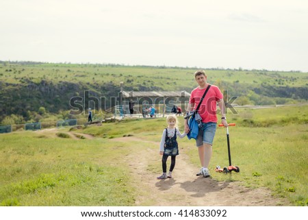 Father taking his cute young daughter for a walk along a rural pathway in warm sunshine holding her hand as they stroll along, rear view
