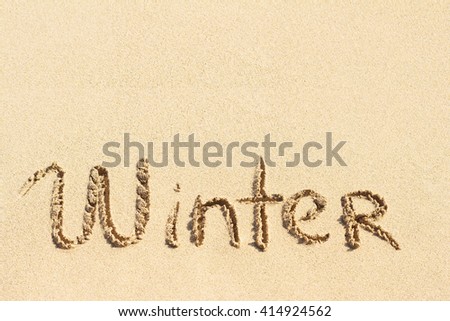 Word Winter handwritten on sandy beach 