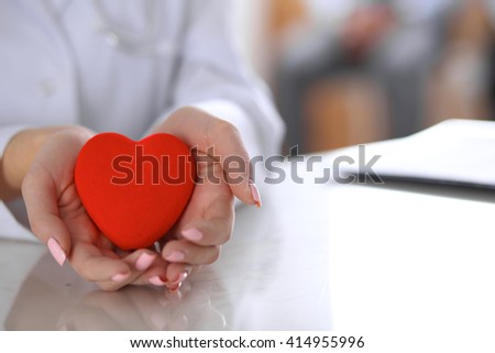 Female doctor with stethoscope holding heart.  Patients couple sitting in the background