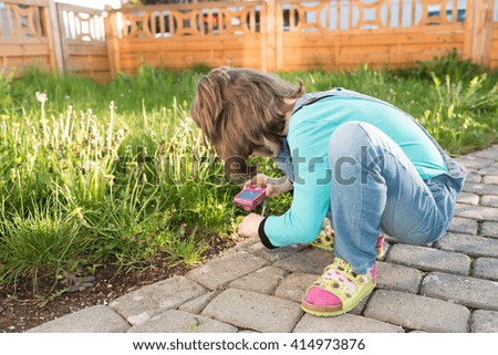 Little cute girl taking photos in the garden with a camera