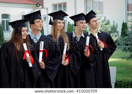 Graduates embrace, enjoy and look forward on the graduation ceremony. Happy graduation day. 5 graduates hold his graduate diplomas in their hands.