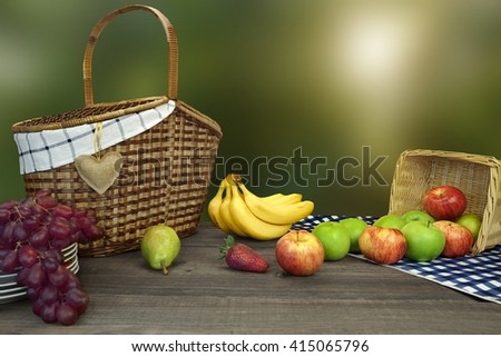 Closeup Of Picnic Basket With Fruits On The Table With Blue Checkered Tablecloth And Summer Garden In The Background