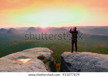 Man photography with phone of  dreamy hilly landscape, spring orange pink misty sunrise in a beautiful valley of rocky mfountains.