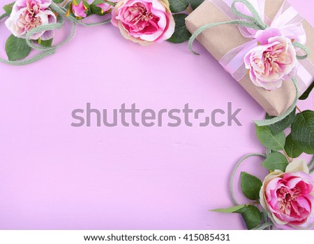 Pale pink feminine background with gift and silk roses on wood table with decorated borders, for Mothers Day, Valentine or feminine birthday or anniversary with copy space. 