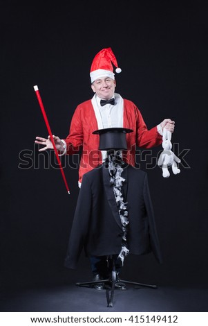 Funny magician with wand and hat at black background
