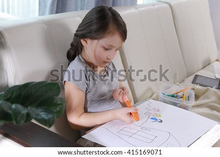 Girl in bright clothing draws a picture of the family. Light room