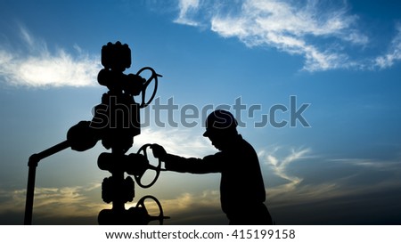 Sunset and silhouette of oilfield worker monitoring wellhead controls in oilfield  Royalty-Free Stock Photo #415199158