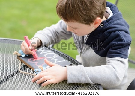 Little boy child drawing a love declaration on small blackboard for his mother on Mother's Day. 