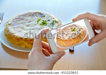 woman taking a picture of a potatoes omelet typical of Spanish cuisine on a wooden table with the smartphone 