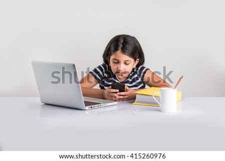 Education at home concept - Cute little Indian/Asian girl using smartphone for texting or taking selfie picture in the middle of studies at home