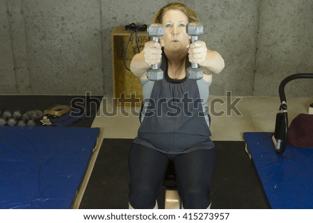 Mature woman in  basement gym using free weights to strengthen upper body.