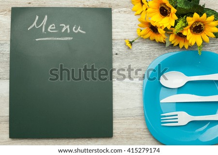 Menu hand written on chalkboard,dish and dining utensil plastic and sun flower on white wooden background