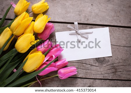 Bright yellow and pink spring tulips  and empty tag on vintage wooden background. Selective focus. Place for text.