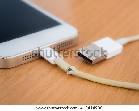 Close of broken charger cable with smart phone on the wooden table