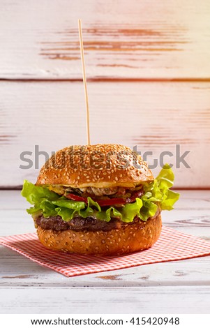 Burger on wooden stick. Big burger laying on napkin. White table with fresh beefburger. Fat and calories.