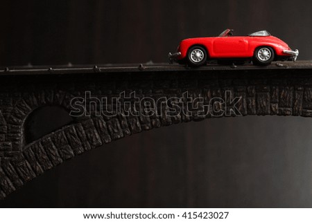 The old and dirty red color miniature toy car put on the model toy bridge represent the transportation and vehicle concept related idea.