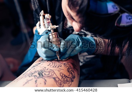 Close up tattoo artist demonstrates the process of getting black tattoo with paint. Master works in black sterile gloves. Master of tattoo fill circuit tattoo. Royalty-Free Stock Photo #415460428