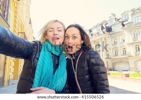 Girlfriends make a self portrait using her phone. Two women friends! Close-up portrait of young girls. Happy woman make picture together and having fun, laughing and make funny faces on camera. Travel