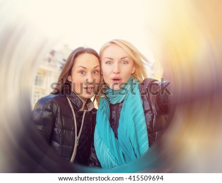 Two women friends! Girlfriends make a self portrait using her phone. Close-up portrait of young girls. Woman make picture together, having fun, laughing and make funny faces on camera. Circular blur.