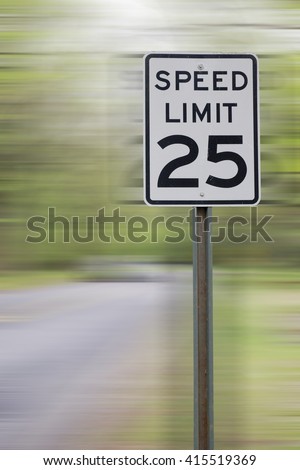 25 MPH SPEED LIMIT SIGH WITH MOTION BLURRED ROAD IN FOREST BACKGROUND