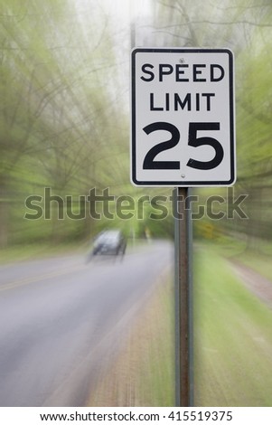 25 MPH SPEED LIMIT SIGH WITH MOTION BLURRED ROAD IN FOREST BACKGROUND