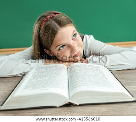 Fantasy pupil looking up as if daydreaming or thinking of something pleasant while sitting at the desk with open book. Photo of teen school girl, creative concept with Back to school theme