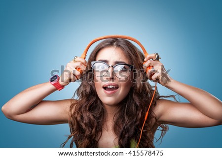 Surprised shocked girl with long curly hair in headphones listening to music. Closeup portrait female on blue background. Human emotion facial expression feeling