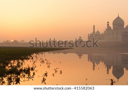 Taj Mahal view with reflection from Yamuna river bank. Picture shot during sunrise with foggy morning.