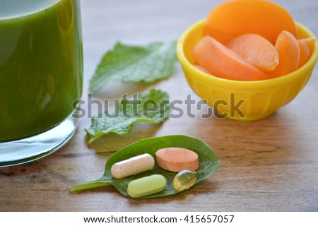 Green detox smoothie, dietary supplements and a serving of apricots on wooden table Royalty-Free Stock Photo #415657057