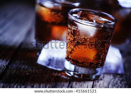 Alcoholic cocktail bourbon cola with whiskey and ice cubes, vintage wooden background, selective focus