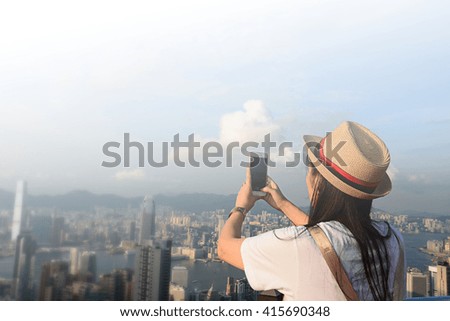 The back view of young hipster girl is taking photo pictures on mobile phone of an amazing view of Hong Kong. Tourism travel concept.