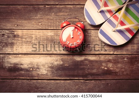 photo of the red clock and colorful sandals on the brown wooden background