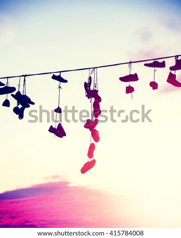 Vintage toned silhouettes of shoes hanging on cable at sunset, teenage rebellion concept.