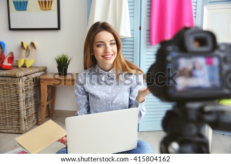 Young female blogger with laptop and book on camera screen Royalty-Free Stock Photo #415804162