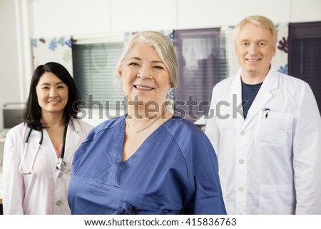 Confident Female Nurse Smiling With Doctors In Clinic