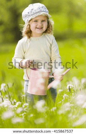 Sweet little toddler watering flowers with a pink water can on a garden or meadow.