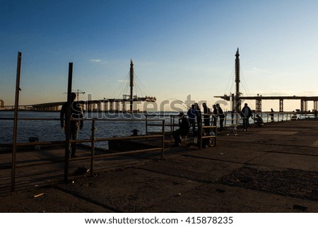 a group of fishermen catch fish before connecting under construction bridge on the Bay at sunset
