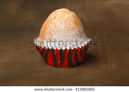 Muffin covered by powdered sugar stands on a wooden background