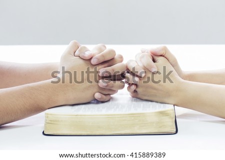 praying hands of two people on one bible on white table background