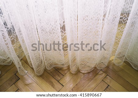 Curtain and floor/Image of a white interwoven curtain hanging on the hardwood floor as seen in the natural window sunlight.